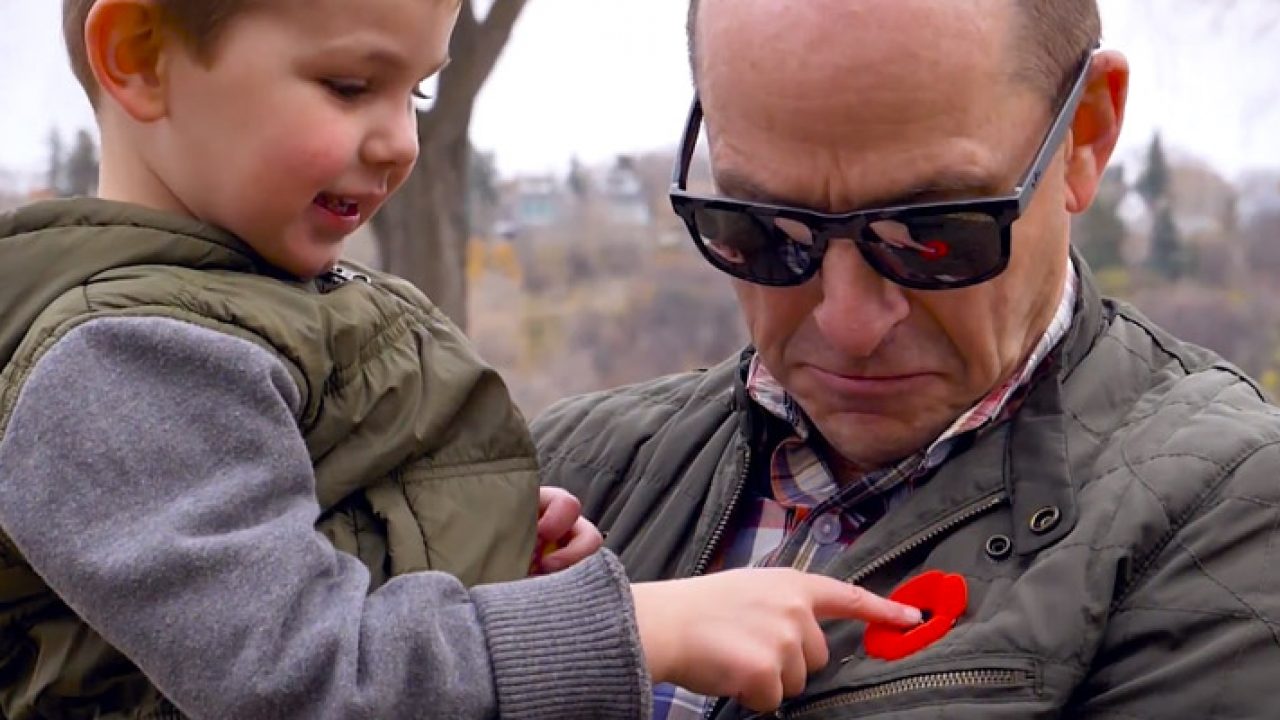 Little boy pointing to a poppy being worn on the lapel of a man who is holding him in his arms