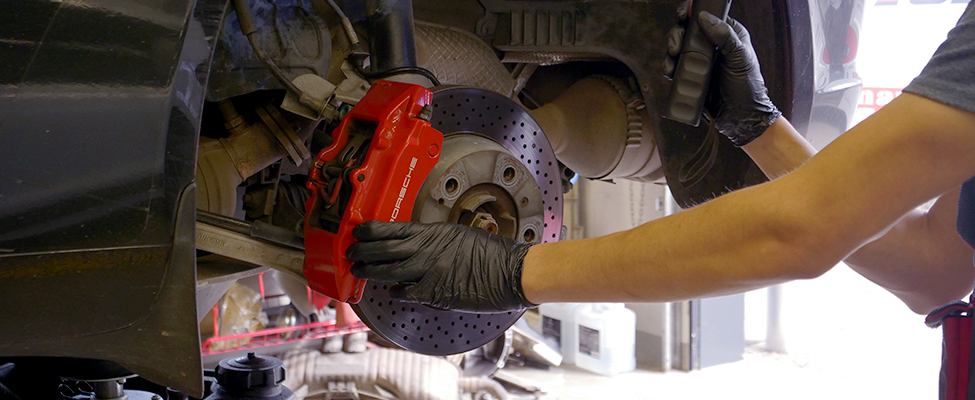 Certified technician inspecting the brakes, drivetrain and suspension components on a Porsche